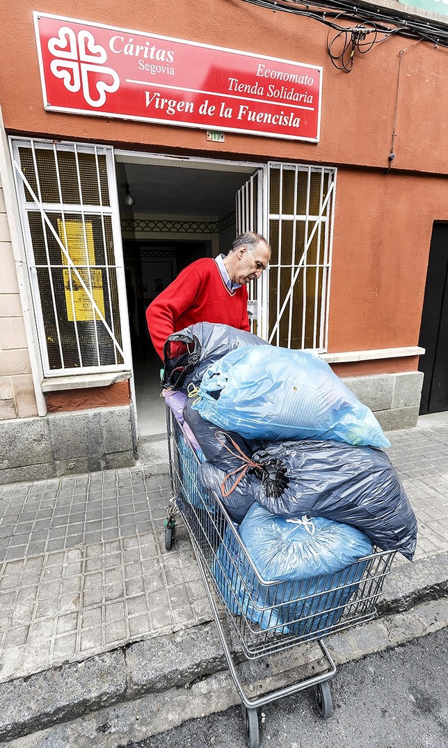 Un voluntario ayuda a introducir en la sede con un carrito varias bolsas repletas de ropa. 