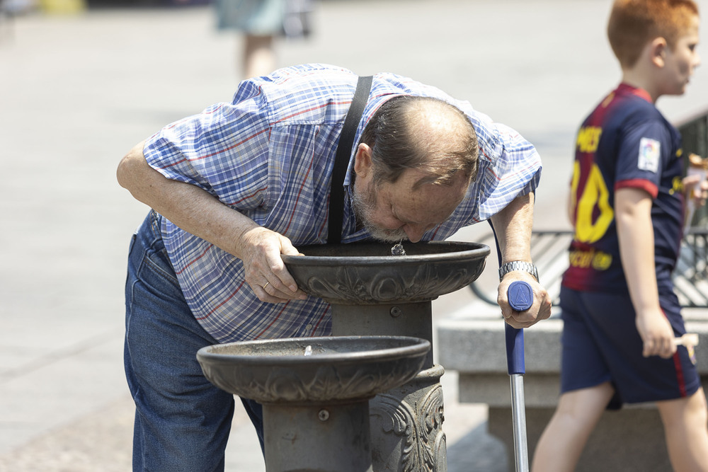 Un hombre se refresca en una fuente de la avenida del Acueducto.